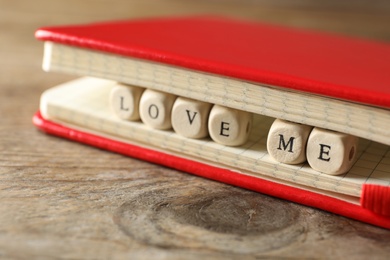 Photo of Notebook and cubes with letters forming phrase Love Me on wooden table, closeup