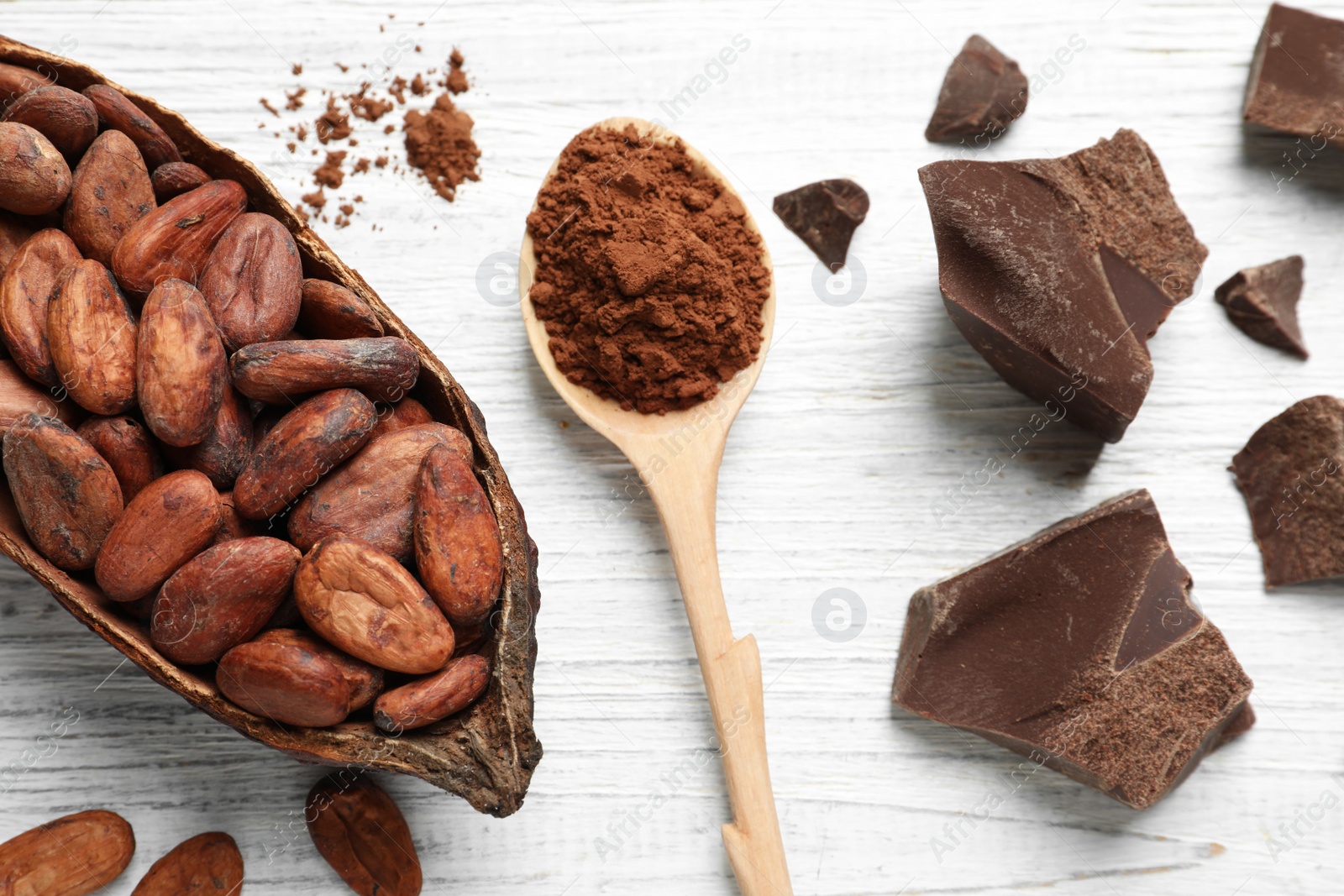 Photo of Flat lay composition with cocoa beans, spoon of powder and chocolate on white wooden table