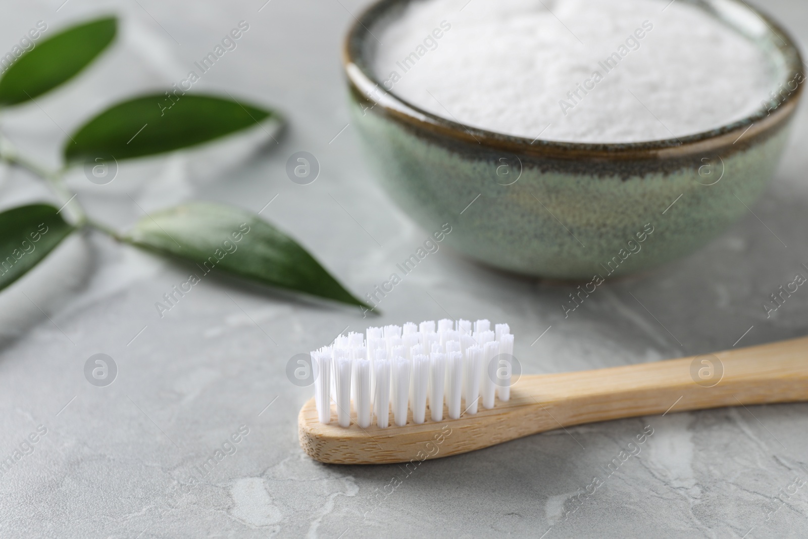 Photo of Bamboo toothbrush and bowl of baking soda on light gray marble table, closeup