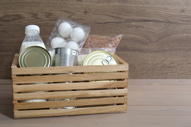 Donation box with food products on wooden table, space for text