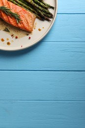 Photo of Tasty grilled salmon with asparagus and spices on light blue wooden table, top view. Space for text