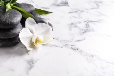 Photo of Spa stones, beautiful orchid flower and bamboo sprout on white marble table, space for text