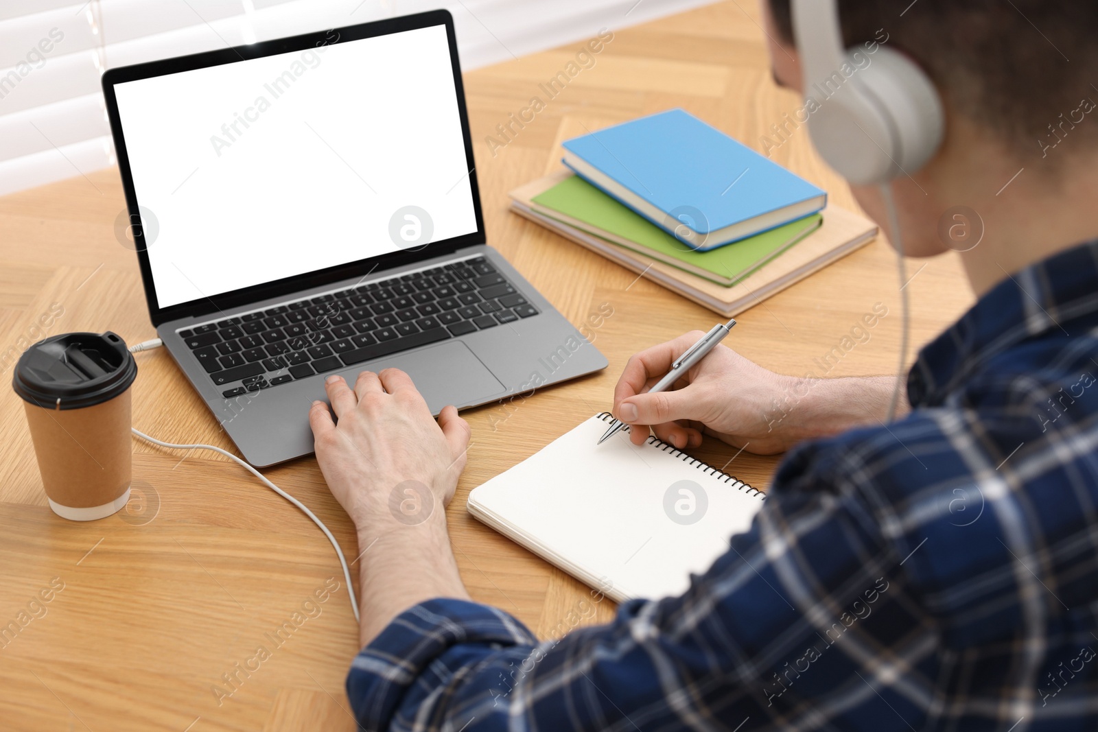 Photo of E-learning. Man taking notes during online lesson at table indoors, closeup