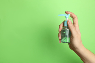 Photo of Woman holding antiseptic gel on green background, closeup. Space for text