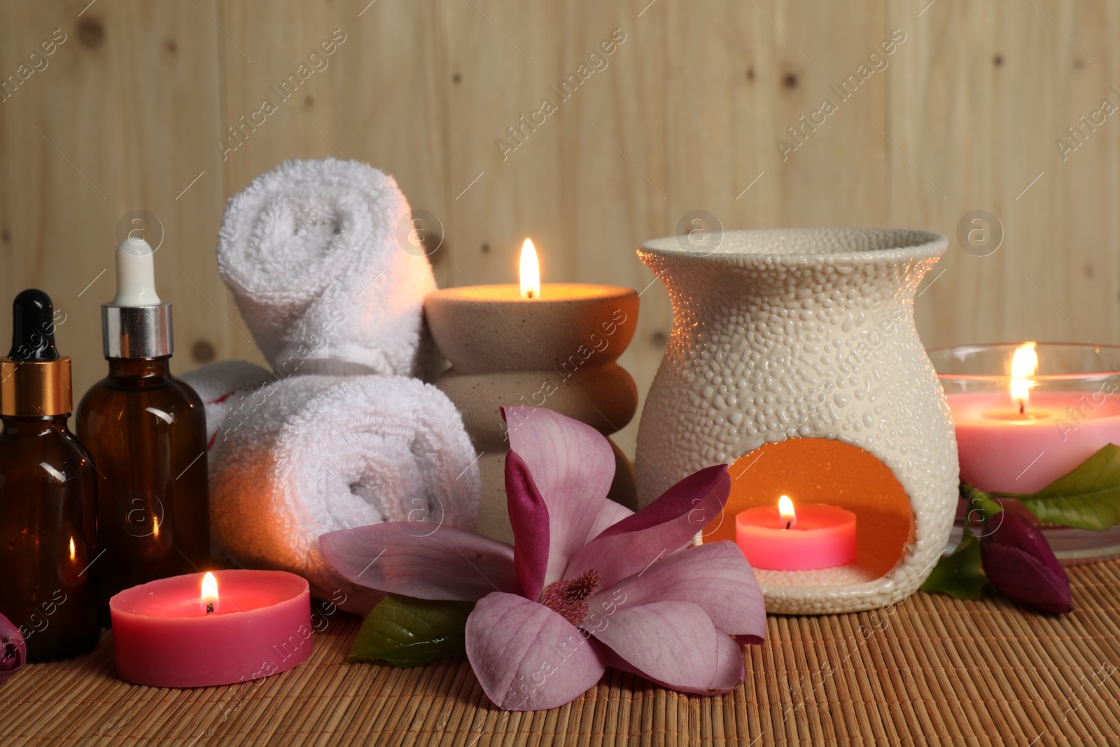 Photo of Aromatherapy. Scented candles, bottles, flower and towels on bamboo mat