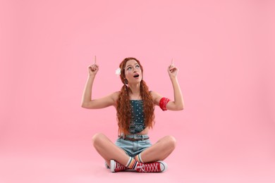 Beautiful young hippie woman pointing upwards on pink background