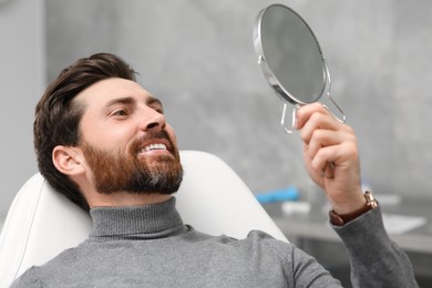 Photo of Man looking at his new dental implants in mirror indoors
