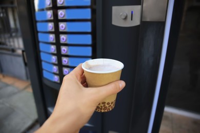 Man holding paper cup with hot drink near coffee vending machine, closeup