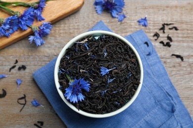 Bowl with dry tea leaves and cornflowers on wooden table, flat lay