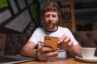 Handsome man using smartphone at table in cafe, focus on hands