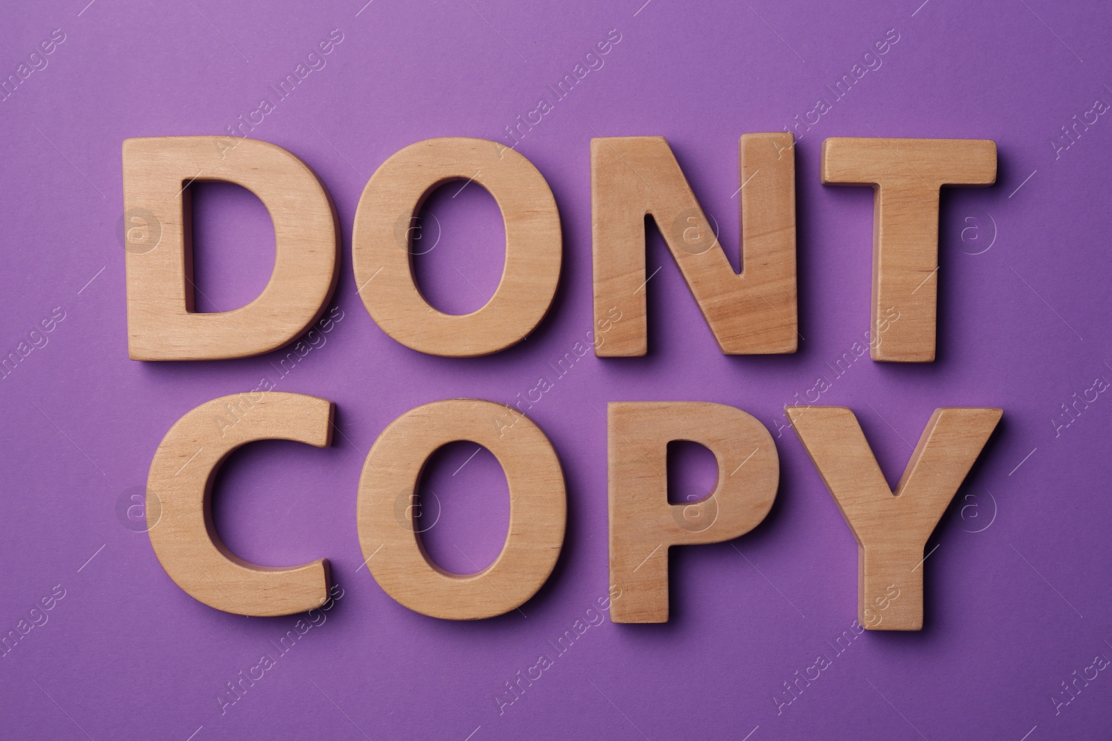 Photo of Plagiarism concept. Phrase Don't Copy made of wooden letters on violet background, top view