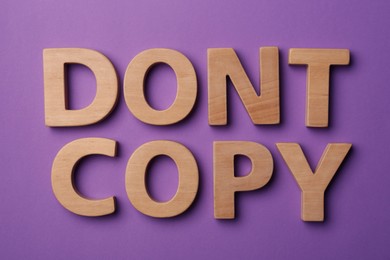 Photo of Plagiarism concept. Phrase Don't Copy made of wooden letters on violet background, top view