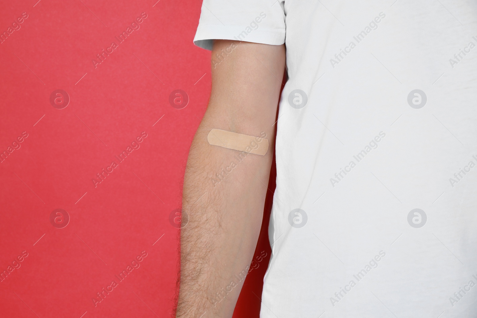 Photo of Blood donation concept. Man with adhesive plaster on arm against red background, closeup. Space for text