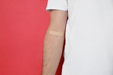 Photo of Blood donation concept. Man with adhesive plaster on arm against red background, closeup. Space for text