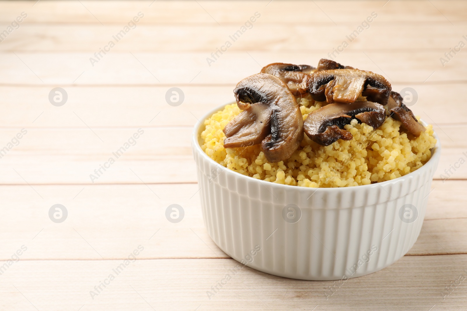 Photo of Tasty millet porridge and mushrooms in bowl on light wooden table, closeup. Space for text