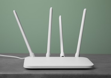 Photo of New modern Wi-Fi router on grey table near green wall