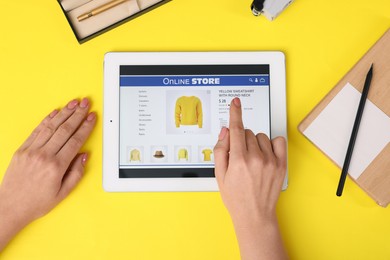 Woman with tablet shopping online on yellow background, top view