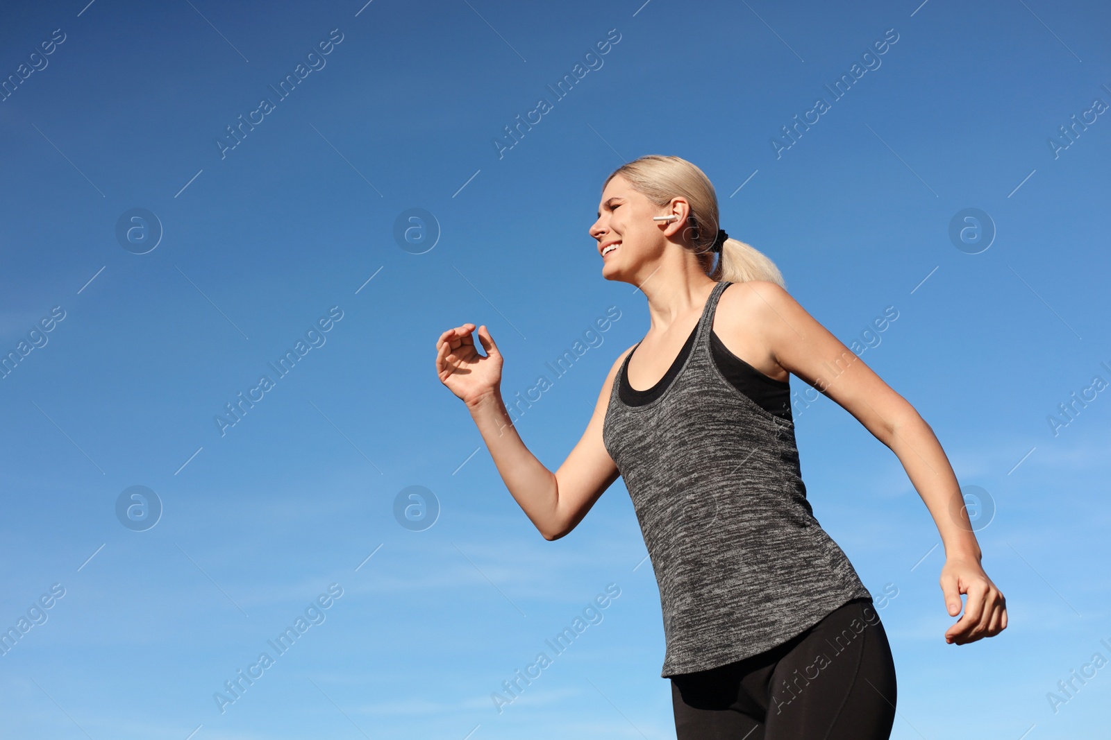 Photo of Woman listening to music while running outdoors in morning, low angle view. Space for text