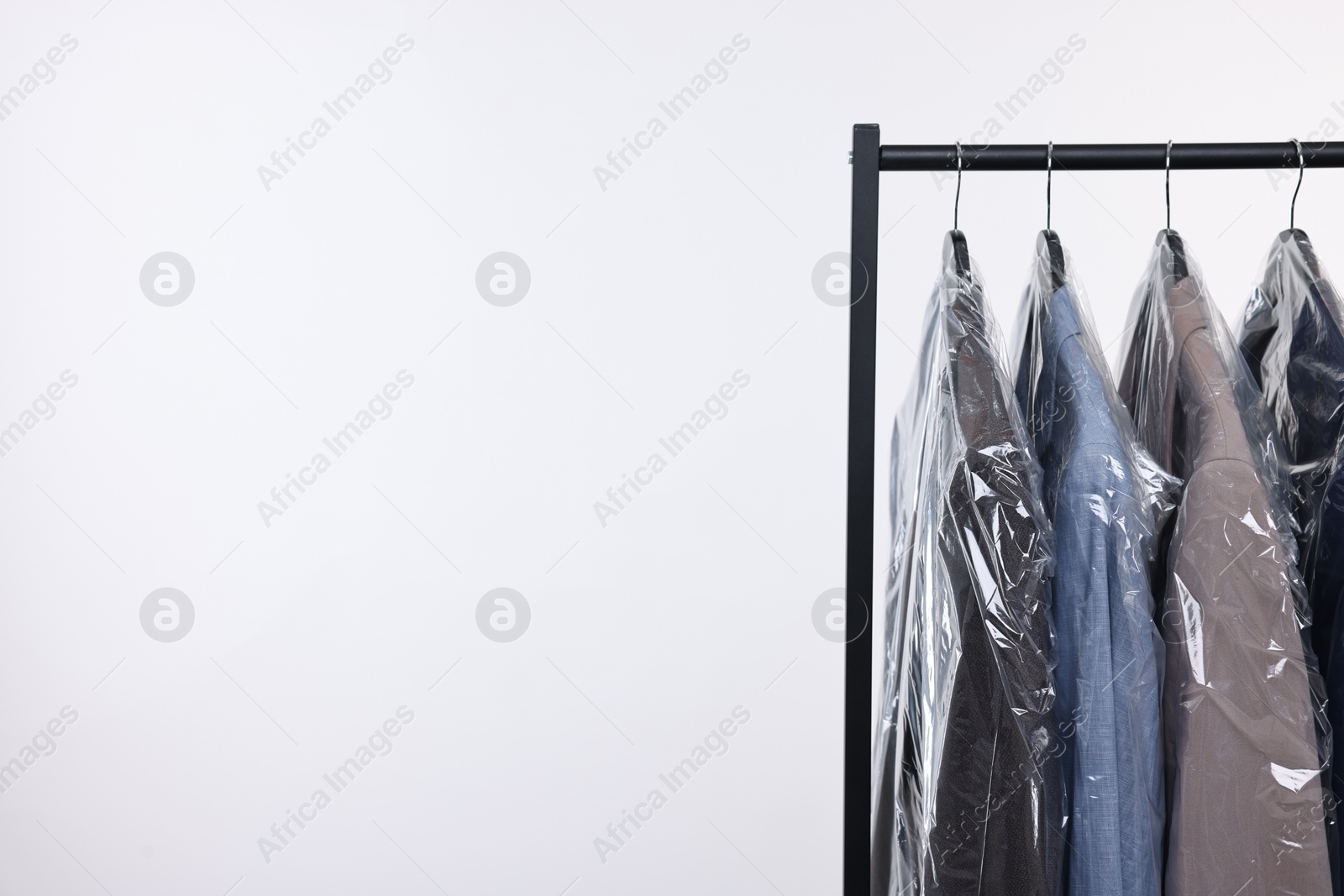 Photo of Dry-cleaning service. Many different clothes in plastic bags hanging on rack against white background, space for text