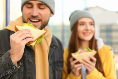 Happy young couple with sandwiches on city street