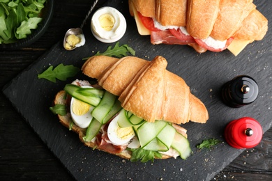 Photo of Tasty croissant sandwiches with bacon on dark background, top view
