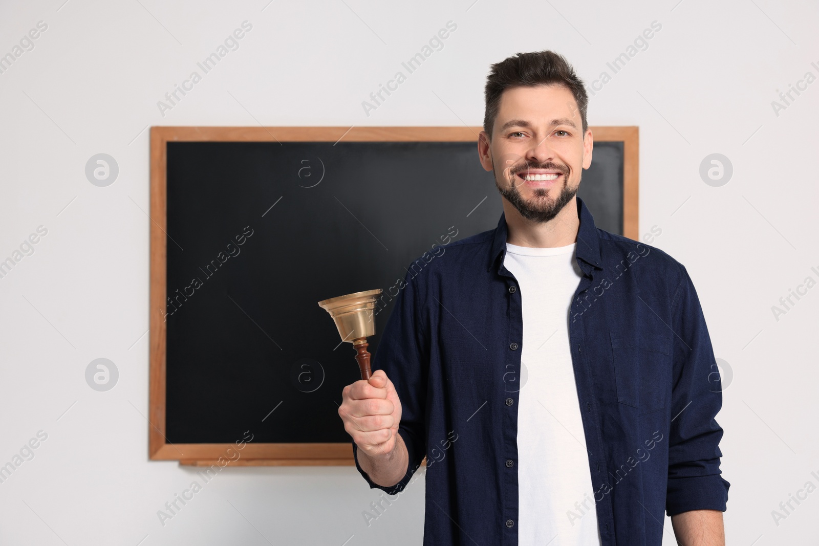 Photo of Teacher with school bell near black chalkboard indoors. Space for text