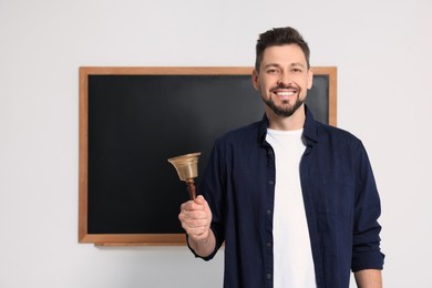 Photo of Teacher with school bell near black chalkboard indoors. Space for text