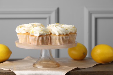 Photo of Delicious lemon cupcakes with white cream and lemons on table