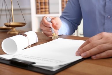 Male notary stamping document at table in office, closeup