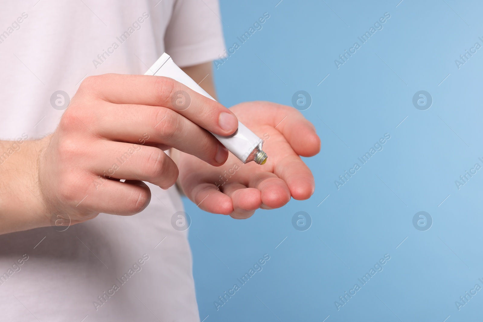 Photo of Man applying ointment from tube onto his hand on light blue background, closeup. Space for text
