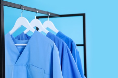 Photo of Medical uniforms on metal rack against light blue background, closeup