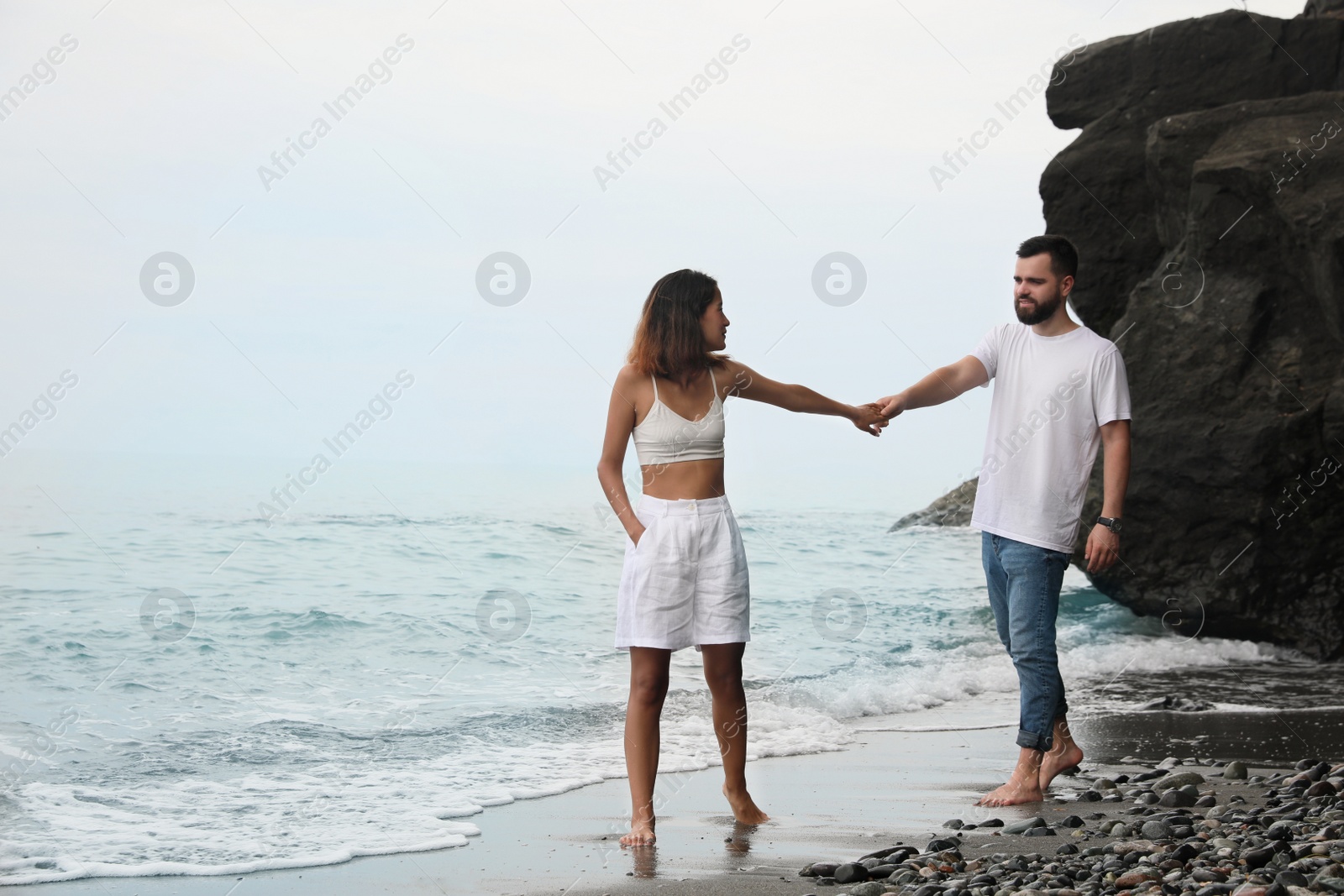 Photo of Young couple walking on beach near sea. Space for text