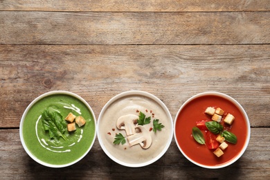 Various cream soups in bowls and space for text on wooden background, top view