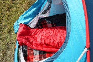 Photo of Red sleeping bag in camping tent on green grass outdoors, above view