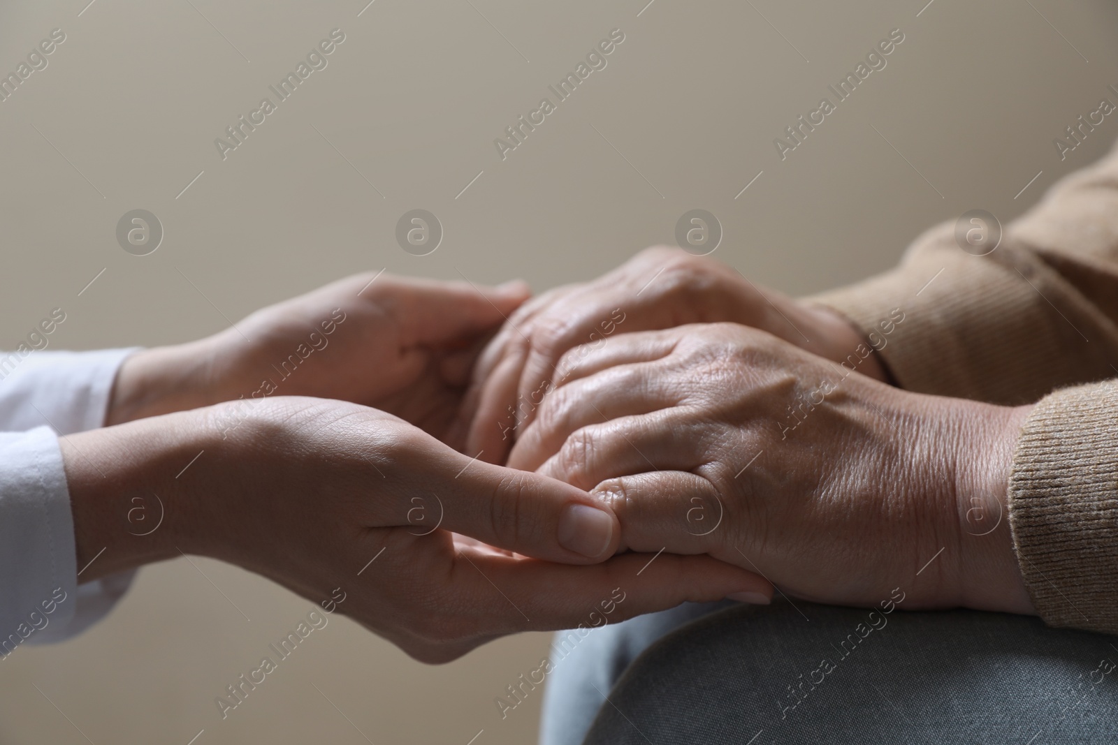 Photo of Woman holding hands with her mother on beige background, closeup