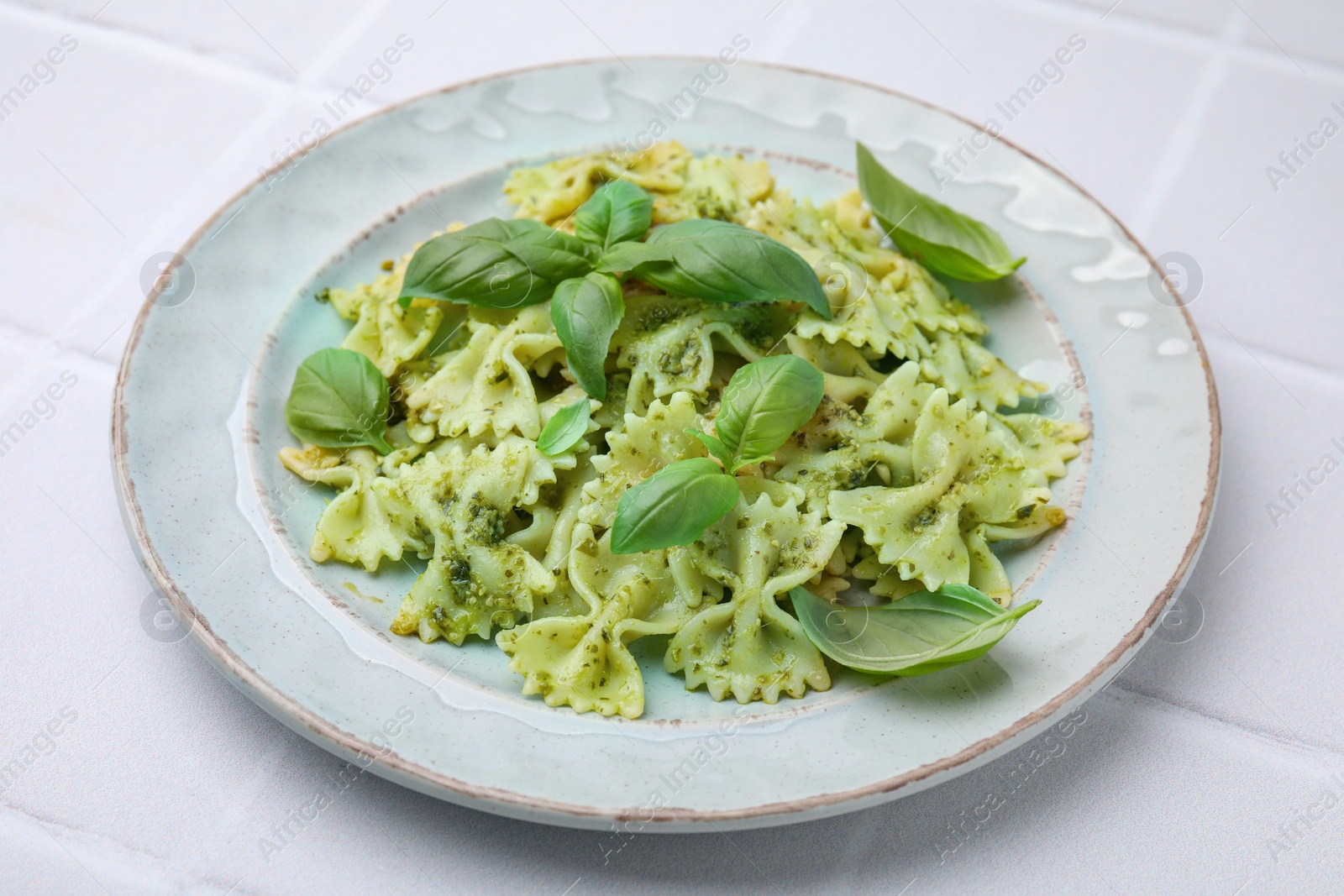 Photo of Delicious pasta with pesto sauce and basil on white tiled table, closeup