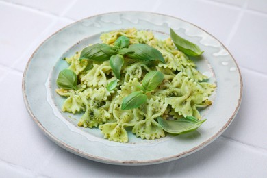 Delicious pasta with pesto sauce and basil on white tiled table, closeup