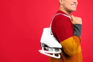 Photo of Happy man with ice skates on red background, closeup. Space for text