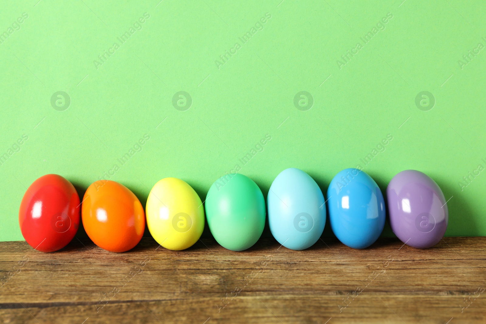 Photo of Easter eggs on wooden table against green background, space for text