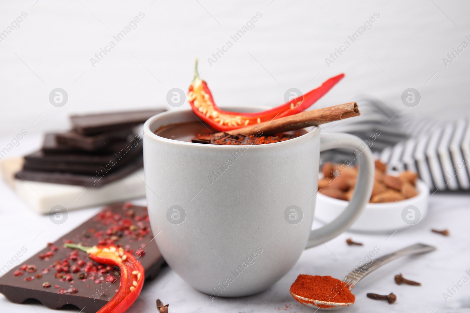 Photo of Cup of hot chocolate with chili pepper and cinnamon on white marble table