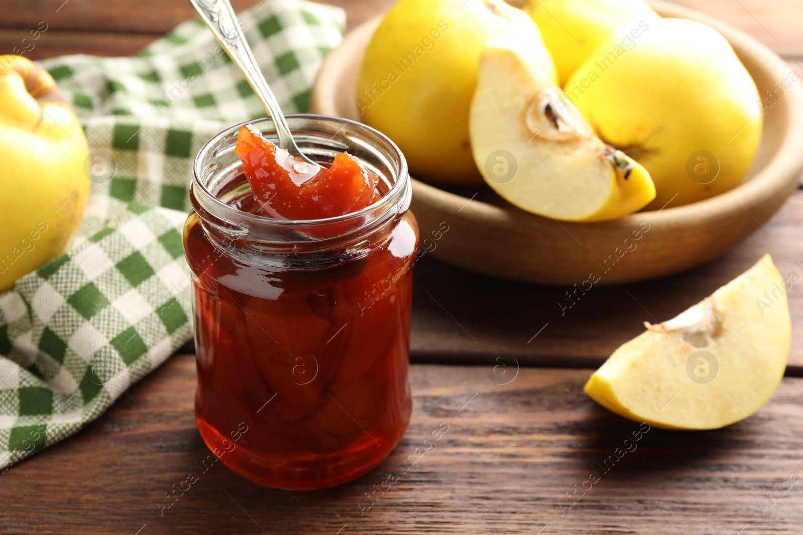 Photo of Tasty homemade quince jam in jar, spoon and fruits on wooden table, closeup