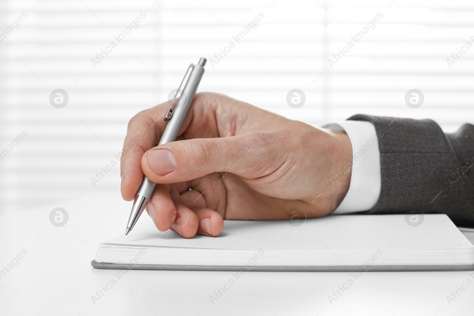 Photo of Man writing in notebook at white table, closeup