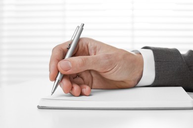 Man writing in notebook at white table, closeup