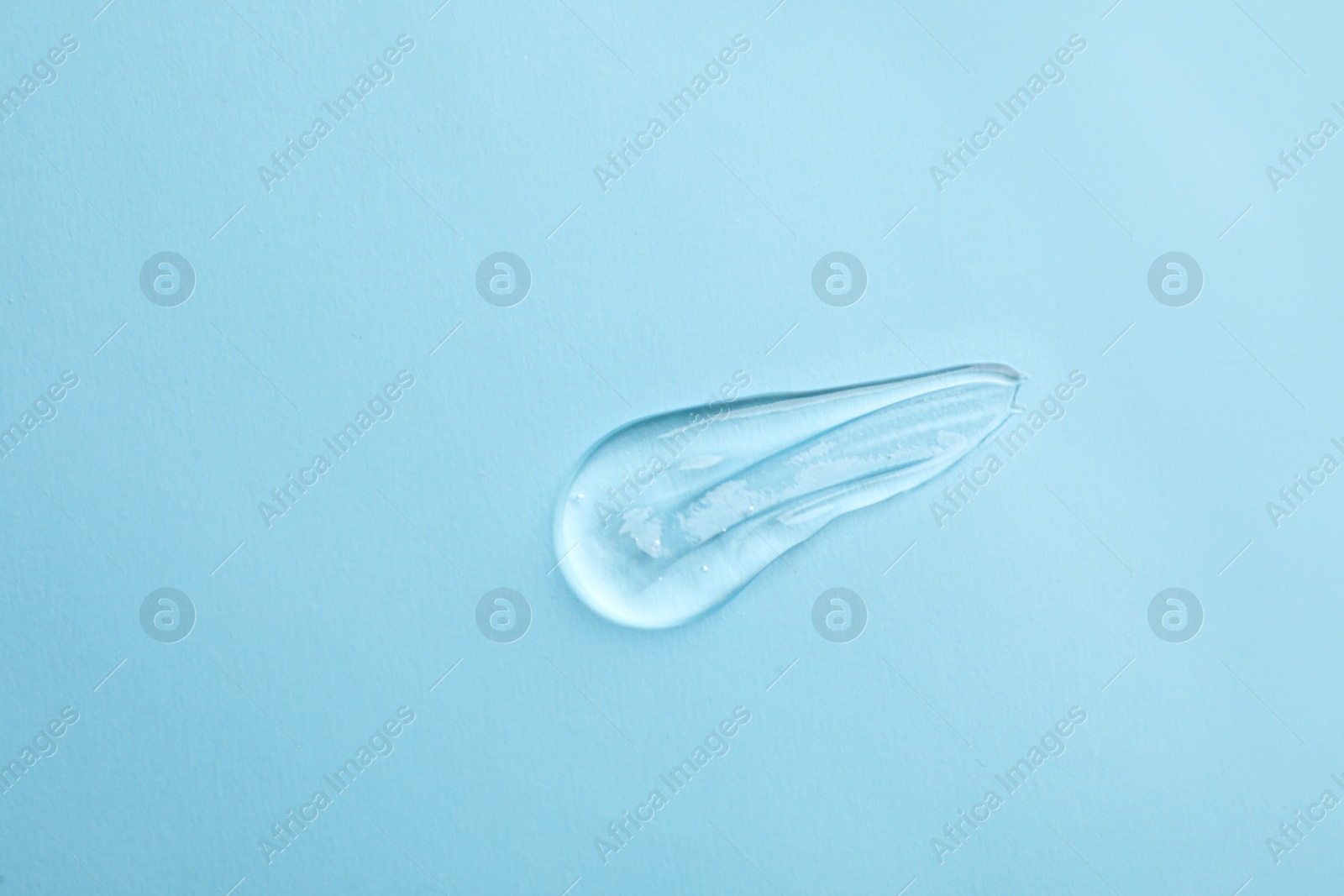 Photo of Smear of transparent ointment on light blue background, top view