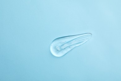 Photo of Smear of transparent ointment on light blue background, top view