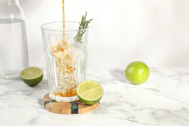Photo of Pouring coffee into glass with ice cubes at white marble table. Space for text