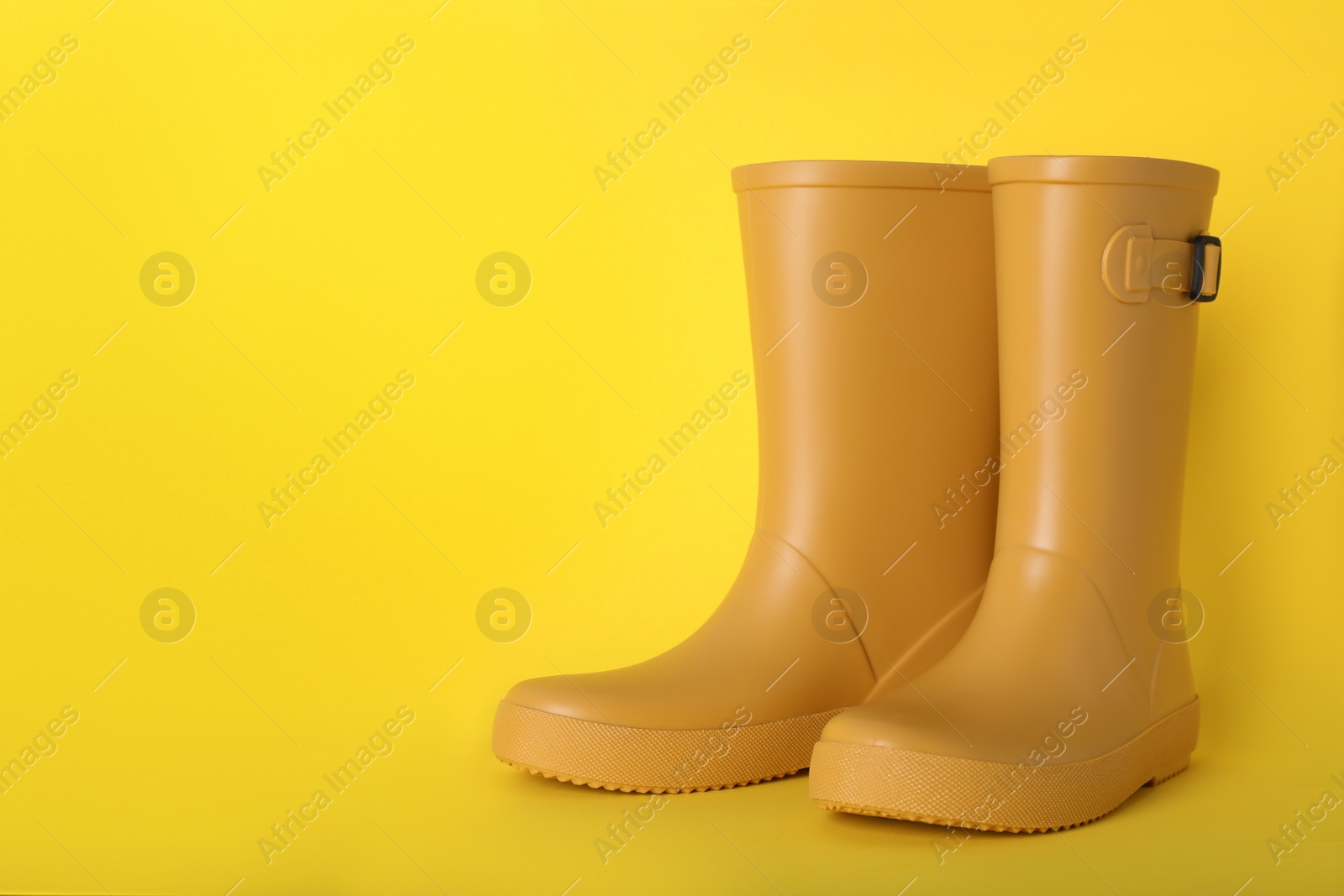 Photo of Pair of bright rubber boots on yellow background.  Space for text
