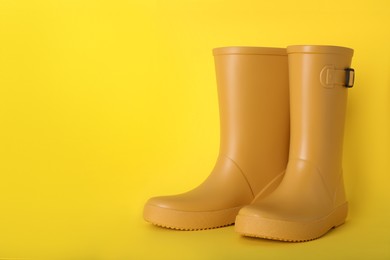 Photo of Pair of bright rubber boots on yellow background.  Space for text