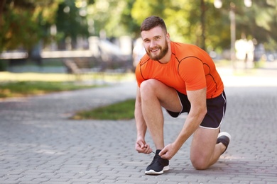 Photo of Young man tying shoelaces before running in park on sunny day