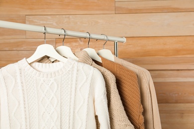 Collection of warm sweaters hanging on rack against wooden background